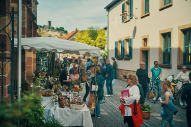 Ein lebhafter Markt in einer charmanten Straße mit vielen Menschen und Ständen. Die Atmosphäre ist freundlich und einladend, während die Besucher stöbern und einkaufen.