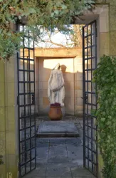 Ein hübscher Garten mit einer Statue im Hintergrund. Die Statue steht in einem Raum, der von einem schmiedeeisernen Tor umgeben ist.