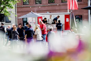 Eine lebhafte Menschenmenge an einem Imbissstand im Freien. Die Leute sprechen miteinander und genießen das Essen in einer angenehmen Atmosphäre.