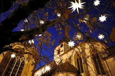 Ein schöner Baum mit leuchtenden Sternen hängt vor einer Kirche bei Nacht. Der Himmel ist klar und dunkelblau.