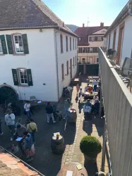 Ein belebter Innenhof mit Menschen, die sich versammeln und gemeinsam Zeit verbringen. Die Umgebung ist hell und einladend, mit Tischen und Stühlen unter freiem Himmel.