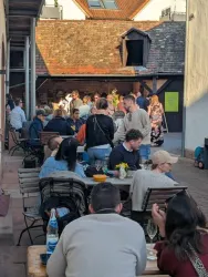 Ein belebter Innenhof mit mehreren Tischen und Menschen, die sich unterhalten. Die Atmosphäre ist entspannt und fröhlich.