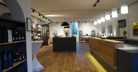 Ein modernes Geschäft mit Holzfußboden und eleganter Beleuchtung. Es gibt Regale mit Produkten und einen Empfangstresen in der Mitte.