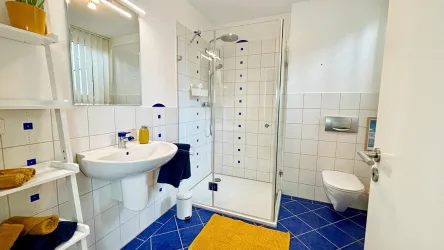 Ein modernes Badezimmer mit blauen Fliesen und einer Dusche. Es gibt ein Waschbecken, eine Toilette und Regale für Handtücher.