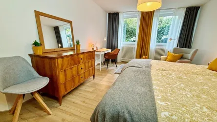 Ein helles Schlafzimmer mit einem großen Bett und Holzmöbeln. Die Fenster lassen natürliches Licht herein, und der Raum ist gemütlich und einladend.