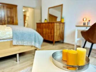 Ein gemütliches Schlafzimmer mit einem Holzschrank und einem Bett. Auf einem Tisch stehen gelbe Kerzen in einer silbernen Schale.