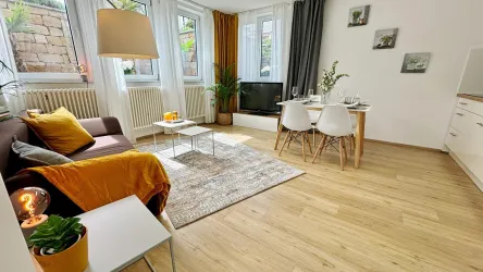 Ein modernes Wohnzimmer mit einer gemütlichen Couch und einem Tisch. Große Fenster lassen viel Licht herein und sorgen für eine angenehme Atmosphäre.