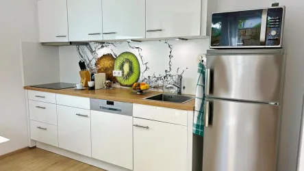Eine moderne Küche mit weißen Schränken und einem Holzarbeitsblatt. An der Wand ist ein bunter Fruchtprint zu sehen, und die Edelstahlküchengeräte verleihen einen eleganten Look.