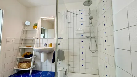 Ein modernes Badezimmer mit einer Dusche und weißen Fliesen. Das Design ist freundlich und hell, mit einem blauen Boden und einer offenen Regablösung.