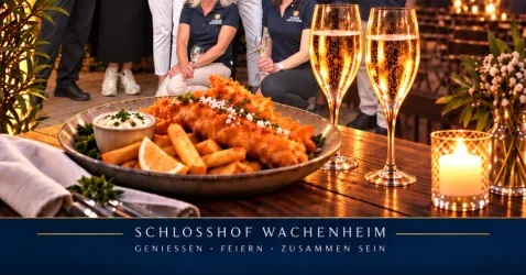 Ein sorgfältig angerichteter Teller mit knusprigem Fisch und Pommes, begleitet von Dips. Im Hintergrund stehen fröhliche Gäste und Gläser mit Sekt.
