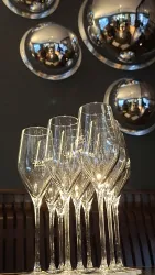 Eine Gruppe eleganter Sektgläser steht auf einem Tisch. Im Hintergrund spiegeln sich runde Wandobjekte.