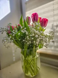 Ein schöner Blumenstrauß mit rosa Tulpen und zarten weißen Blüten. Er steht in einer klaren Vase und bringt Farbe in den Raum.