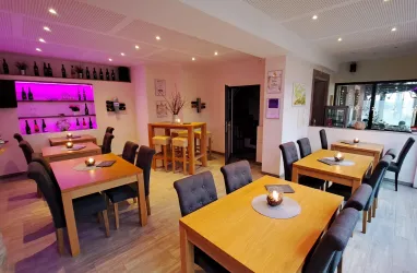 Ein modernes Restaurant mit hellen Holztafeln und bequemen Stühlen. Die Wände sind in sanften Farben gestaltet, und sanftes Licht schafft eine einladende Atmosphäre.