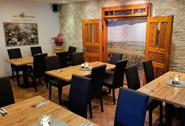 Ein gemütliches Restaurant mit Holztischen und schwarzen Stühlen. Die Wände sind mit Stein und einem dekorativen Bild geschmückt.