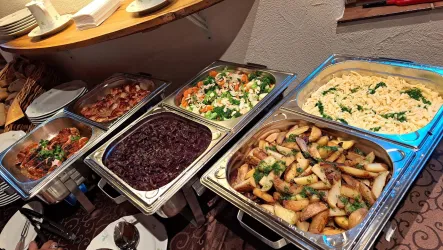 Ein reichhaltiges Buffet mit verschiedenen Gerichten. Zu sehen sind Fleisch, Salate, Kartoffeln und eine cremige Beilage.