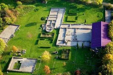 Eine Luftaufnahme von historischen Ruinen in einer grünen Landschaft. Die Strukturen sind klar sichtbar und von Bäumen umgeben.