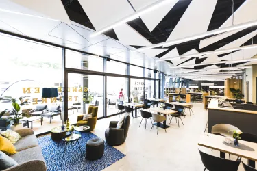 Ein modernes Café mit großen Fenstern und stilvollen Möbeln. Helle Farben und kreative Deckenlichter schaffen eine einladende Atmosphäre.