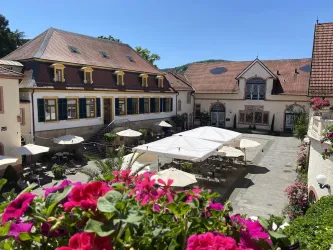 Ein malerischer Innenhof mit Tischen und Sonnenschirmen. Umgeben von historischen Gebäuden und blühenden Blumen.