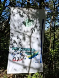 Ein Banner des Pfälzerwald-Vereins zeigt Informationen über Wandern und Natur. Der Hintergrund umfasst Bäume und Pflanzen im Wald.
