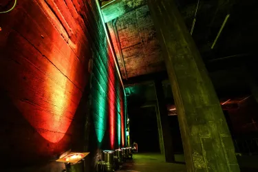 Eine moderne Innenarchitektur mit beleuchteten Wänden in rot und grün. Der Raum hat eine industrielle Atmosphäre mit Betonpfeilern.