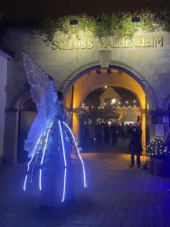 Ein festlich beleuchteter Eingang zum Schloss Wachenheim. Vor dem Tor steht eine Person in einem leuchtenden Kostüm.