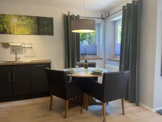 Ein gemütlicher Essbereich mit einem runden Tisch und zwei Stühlen. Die Fenster lassen viel Licht herein und bieten Ausblick auf die Natur.