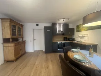 Eine moderne Küche mit dunklen Schränken und Holzdetails. Der Essbereich ist gemütlich mit einem Tisch und gedecktem Geschirr.