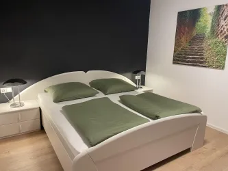 Ein modernes Schlafzimmer mit einem großen, bequemen Bett und grünen Bettwäsche. An der Wand hängt ein Bild von einer Treppe in der Natur.