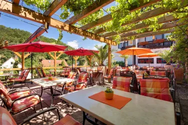 Ein einladendes Restaurant mit vielen Tischen und bunten Sonnenschirmen. Die Terrasse ist von grünen Pflanzen umgeben und bietet eine entspannte Atmosphäre.