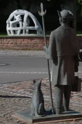 Eine Statue eines Mannes mit einem Stock steht neben einem Hund. Im Hintergrund ist eine weitere Skulptur sichtbar.