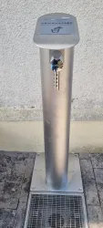Ein Trinkwasserbrunnen aus Edelstahl steht an einer Wand. Er verfügt über einen Wasserhahn und eine Abflussfläche.