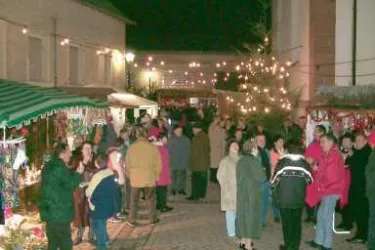 Eine belebte Straße mit Ständen und Lichtern bei Nacht. Viele Menschen genießen das Ambiente und die festliche Atmosphäre.
