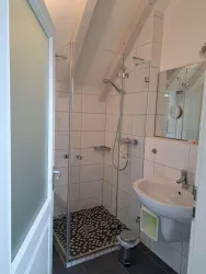 Ein modernes Badezimmer mit einer Duschkabine und einem Waschbecken. Die Wände sind hell gefliest und es gibt einen großen Spiegel.