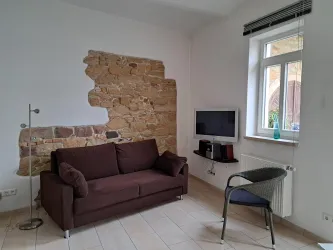 Ein gemütliches Wohnzimmer mit einem braunen Sofa und einem Fernseher an der Wand. Die freiliegende Steinmauer und das Fenster sorgen für eine einladende Atmosphäre.