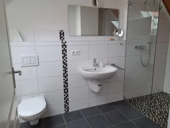 Ein modernes Badezimmer mit einer Dusche, einem Waschbecken und einem WC. Die Wände sind in hellen Fliesen mit einem dekorativen Akzent gestaltet.