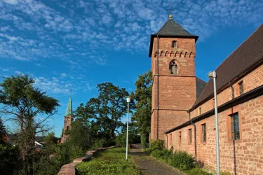 Eine alte Kirche mit zwei Türmen, umgeben von grüner Landschaft und blauem Himmel. Die Architektur zeigt typische Elemente historischer Gebäude.