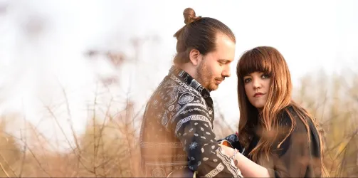 Ein Paar steht in einer natürlichen Umgebung und schaut sich tief in die Augen. Die Atmosphäre ist intim und verträumt.