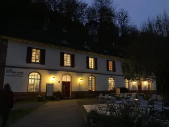 Ein Café in einem historischen Gebäude, beleuchtet im Abendlicht. Umgeben von Bäumen und Stühlen im Freien.