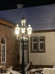 Eine romantische Laterne leuchtet vor einem historischen Gebäude im Schnee. Die Szene vermittelt eine ruhige, winterliche Atmosphäre bei Nacht.