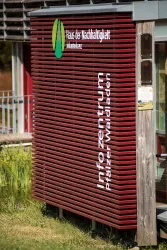 Ein modernes Informationszentrum mit rotbrauner Fassadenverkleidung. Der Name und die Informationen sind deutlich sichtbar.