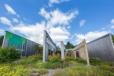Ein modernes, architektonisches Gebäude mit einer Mischung aus Holz und Stein. Es ist von grüner Vegetation umgeben und der Himmel ist klar und blau.