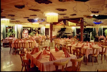 Ein einladendes Restaurant mit zahlreichen Tischen und pinken Tischdecken. Die Wände sind angenehm dekoriert und es gibt Pflanzen sowie eine angenehme Beleuchtung.