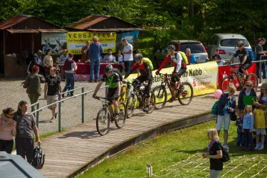 Ein Radrennen mit Teilnehmern auf Mountainbikes. Im Hintergrund sind Zuschauer und Stände sichtbar.
