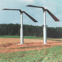 Zwei große Windturbinen stehen auf einem Feld. Im Hintergrund ist eine Waldlandschaft zu sehen.