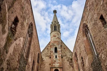 Eine alte Kirche mit einem hohen Turm und historischen Mauern. Der Himmel ist teilweise bewölkt und verleiht der Szene eine ruhige Atmosphäre.