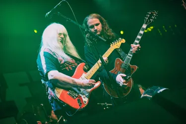 Zwei Musiker spielen auf einer Bühne. Der erste hat eine rote E-Gitarre und der zweite eine akustische Gitarre.