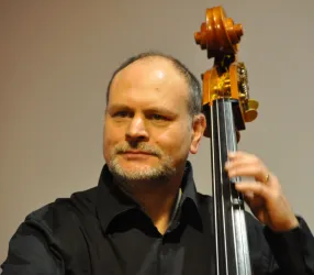 Ein Mann spielt Kontrabass auf der Bühne. Er trägt ein schwarzes Hemd und konzentriert sich auf sein Spiel.