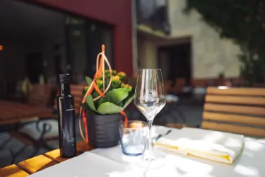 Ein Tisch im Freien mit einem Glas, einer Flasche Öl und einer Pflanze. Die Atmosphäre ist entspannt und einladend.