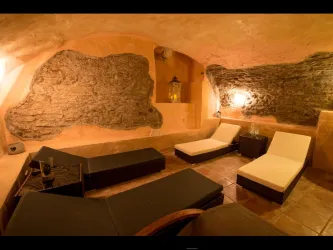 Ein gemütlicher Wellnessbereich mit Liegen und warmem Licht. Die Wände sind aus natürlichem Stein und sorgen für eine entspannte Atmosphäre.