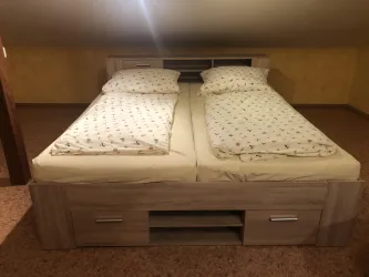 Ein bequemes Doppelbett mit zwei Matratzen und buntem Bettzeug. Der Raum hat eine gemütliche Atmosphäre mit orangefarbenen Wänden.